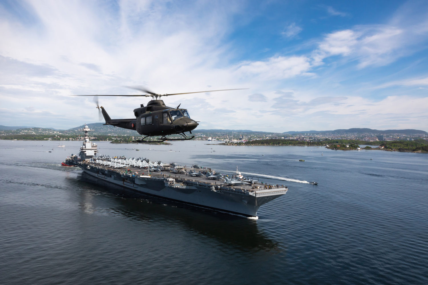 Norge og Oslo fikk i dag, 24 mai 2023 besøk av verdens største militære fartøy, den Amerikanske hangarskipet USS Gerald R. Ford. Bell 412 fra 339 Special Operations Aviation Squadron (SOAS) flyr ved siden av fartøyet i Oslofjorden. // USS Gerald R.Ford sailing in Oslofjorden with NOR Navy vessels as Force Protection