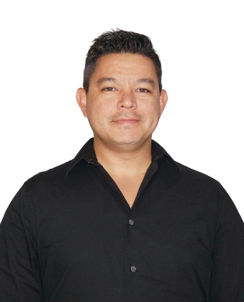 A man with short dark hair is standing in front of a white background. He is wearing a black button-up shirt and looking directly at the camera with a neutral expression.